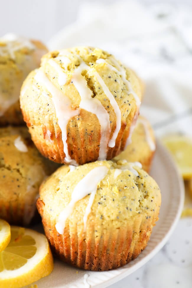 Vertical image of lemon poppy seed muffins piled on a plate with lemon glaze drizzled on top. 