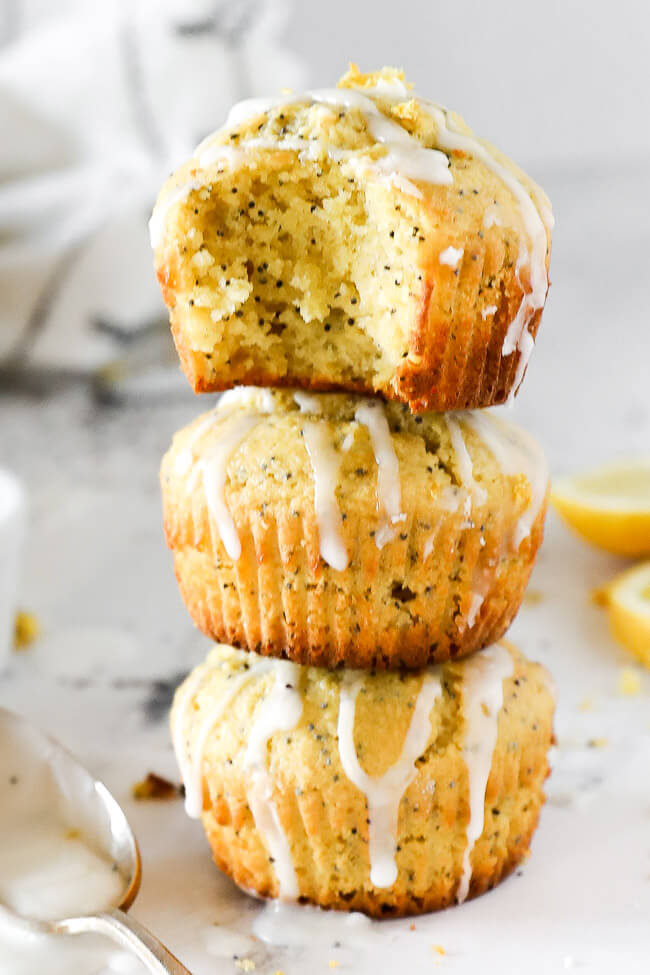 Vertical image of three lemon poppy seed muffins stacked. Top muffin has a bite taken out of it. 