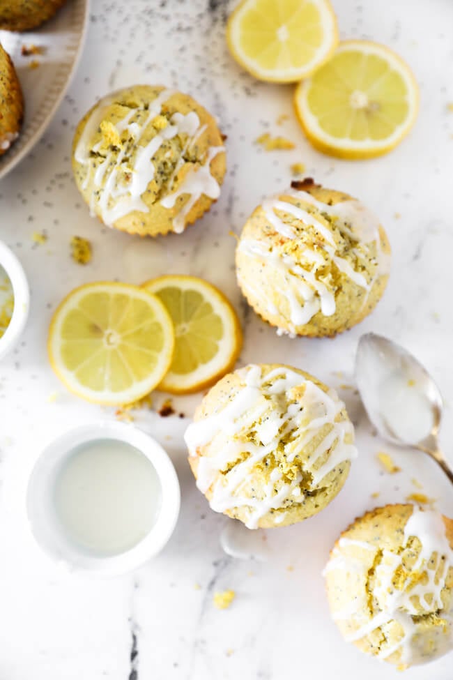 Vertical overhead image of lemon poppy seed muffins making an S shape on marble with extra glaze on the side. 