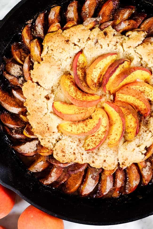 Gluten free peach cobbler in cast iron skillet with extra peaches on top and cinnamon. 