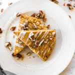 Vertical image of two gluten free and vegan pumpkin scones stacked on a plate with icing and chopped pecans on top.