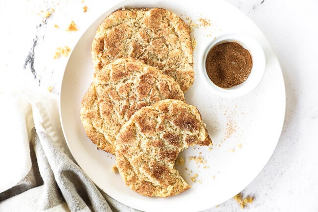 Horizontal image of three gluten free snickerdoodles served on a plate with some cinnamon and sugar on the side. 