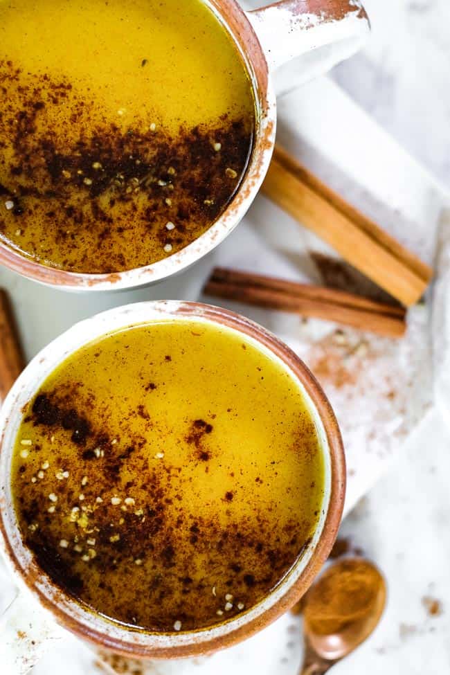 Golden milk latte in two mugs, topped with cinnamon and hemp seeds. 