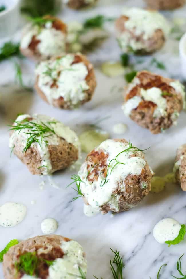 Greek meatballs in a bowl with Tzatziki sauce and fresh dill on top.