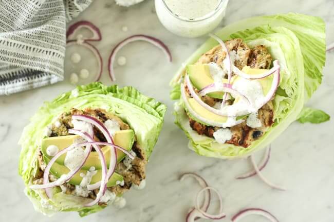 Overhead of two greek turkey burgers laid on top of lettuce and topped with avocado, red onion and tzatziki sauce. 
