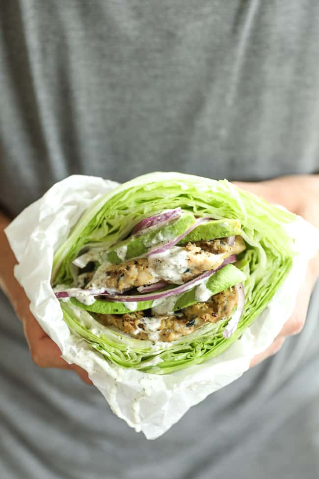 Holding a greek turkey burger wrapped in a lettuce bun and parchment paper. 