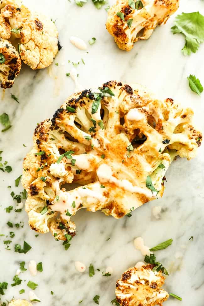 Close up of grilled cauliflower drizzled with sauce and sprinkled with cilantro. 