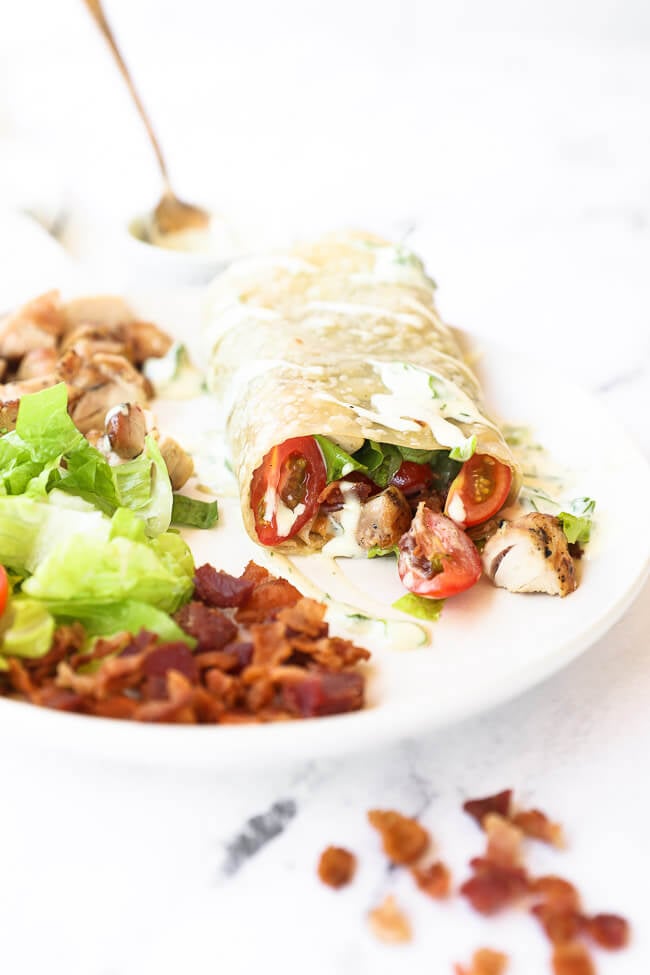 Chicken ranch wrap on a plate with ranch on top and chicken, lettuce and bacon on the side angle image