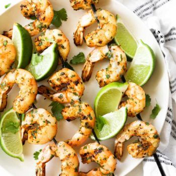 Grilled shrimp kabobs on a plate with lime wedges as a garnish and some fresh chopped cilantro.