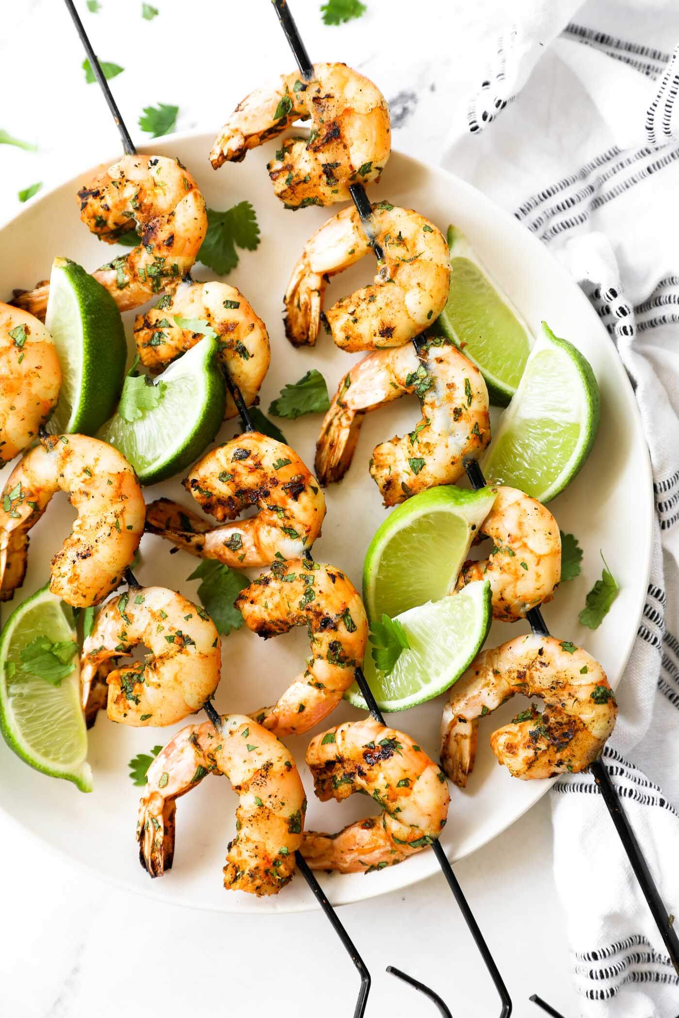 Grilled shrimp kabobs on a plate with lime wedges as a garnish and some fresh chopped cilantro. 