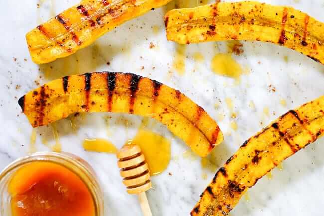Grilled plantains spread out on marble with honey and cinnamon.