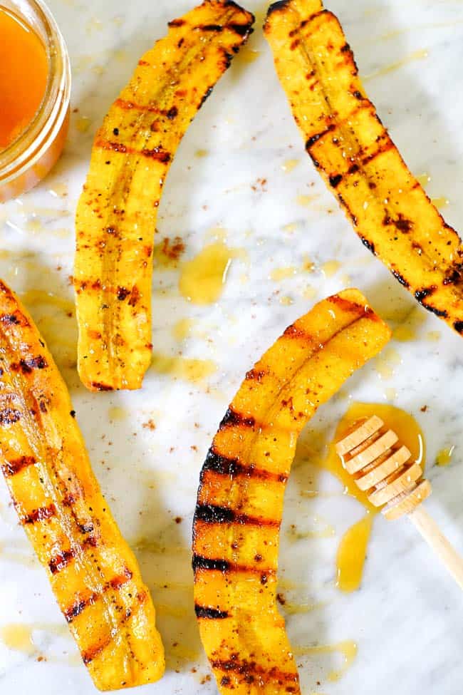 Grilled plantains spread out on marble with honey and cinnamon.