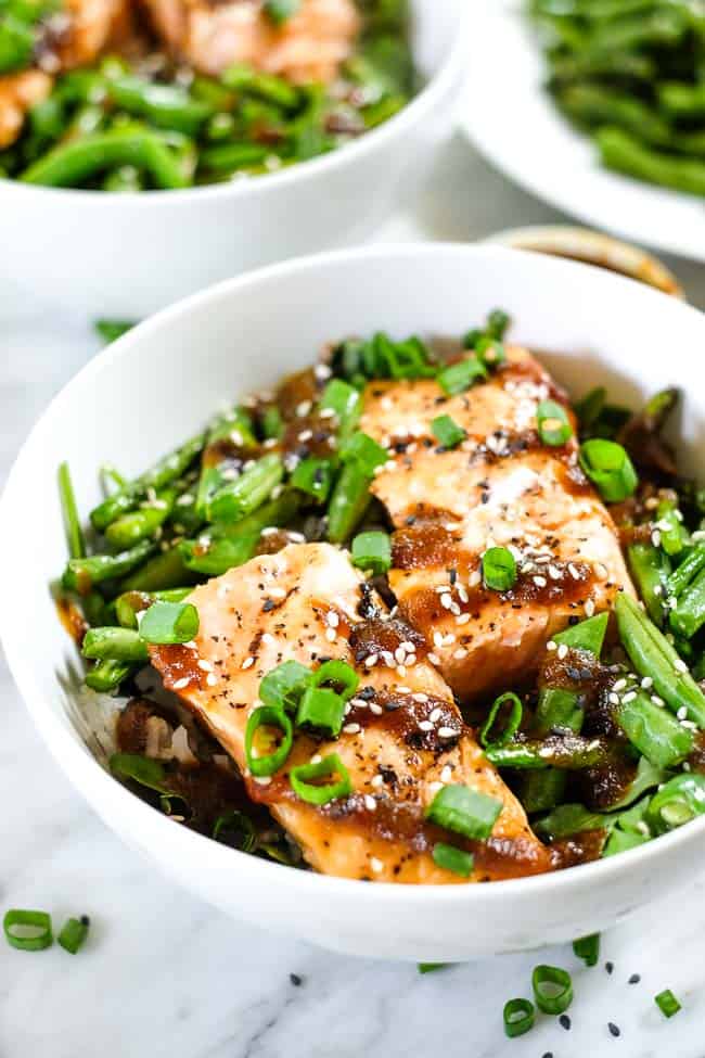 Grilled teriyaki salmon in a bowl with green beans, asparagus, rice and greens. Topped with teriyaki sauce, green onion and sesame seeds. 