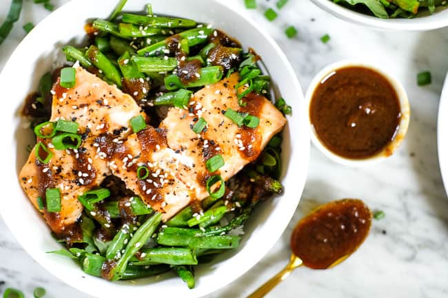 Grilled teriyaki salmon in a bowl with green beans, asparagus, rice and greens. Topped with teriyaki sauce, green onion and sesame seeds. 