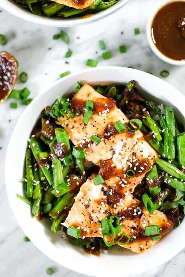 Grilled teriyaki salmon in a bowl with green beans, asparagus, rice and greens. Topped with teriyaki sauce, green onion and sesame seeds. 