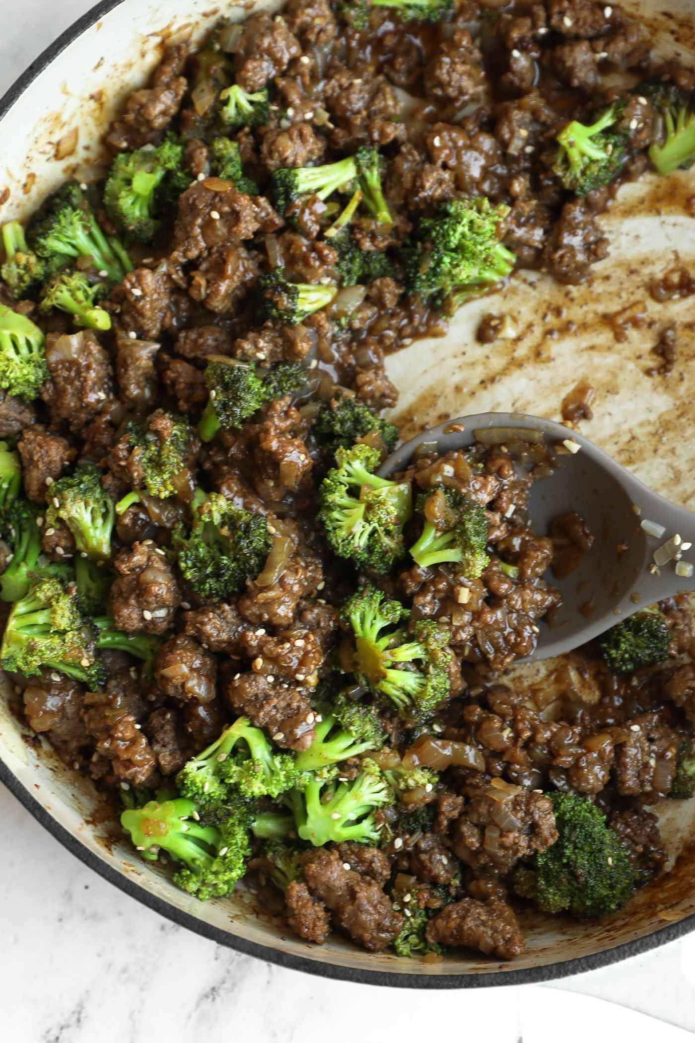 Ground beef, broccoli florets, and savory sauce come together in this easy one pan broccoli stir fry, all mixed in a large skillet with a serving spoon resting inside.
