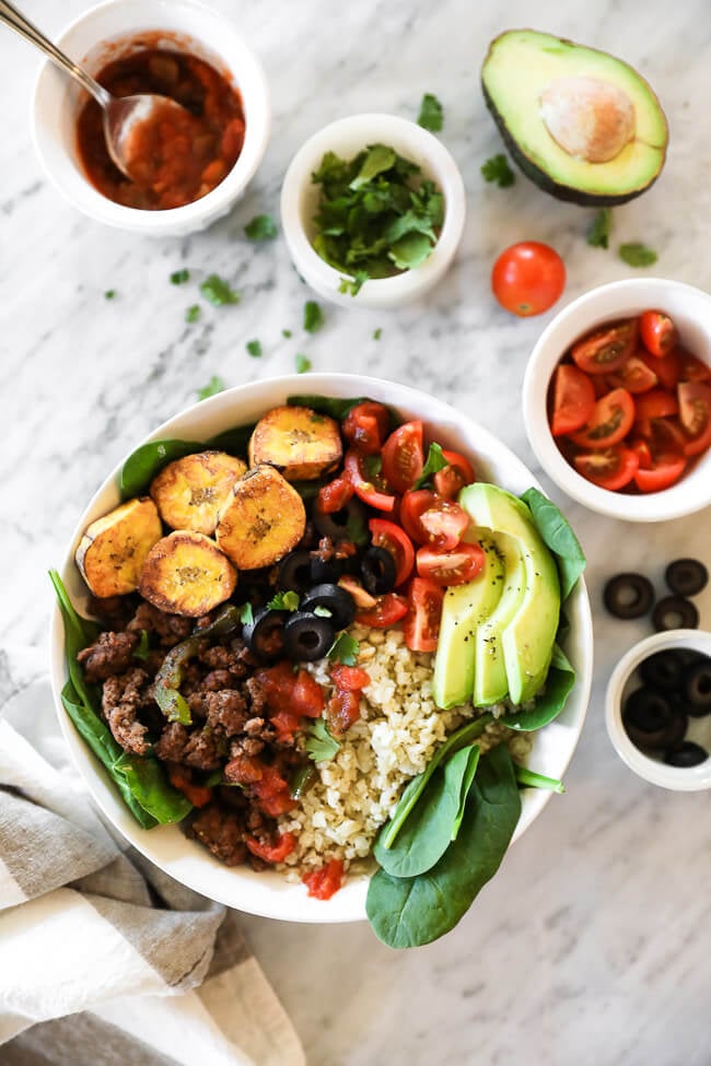 ground beef taco bowl with greens, plantains and cauli rice overhead image with toppings around bowl