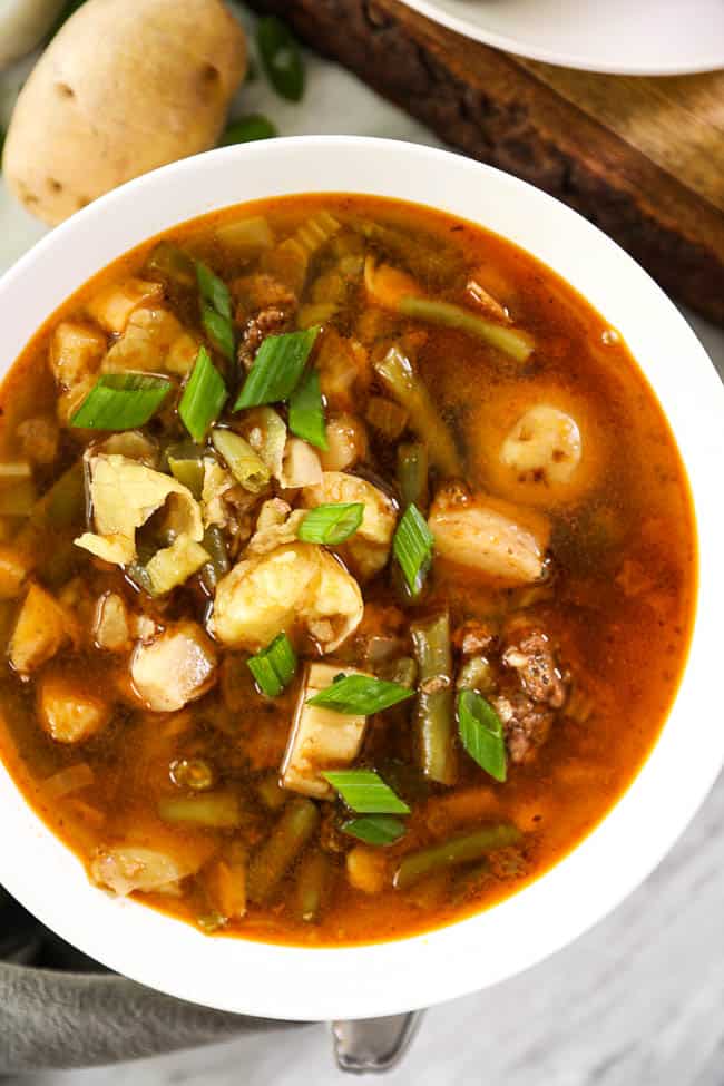 Overhead image of hamburger soup in a bowl with potatoes, mushrooms and chopped green onions