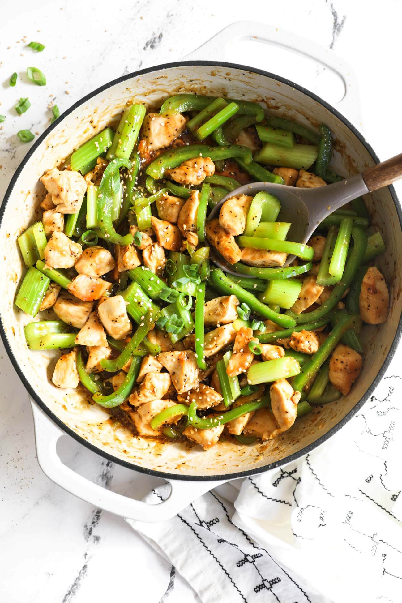 Black pepper chicken stir fry with celery and green bell pepper in a pan with sauce and a spoon scooping in