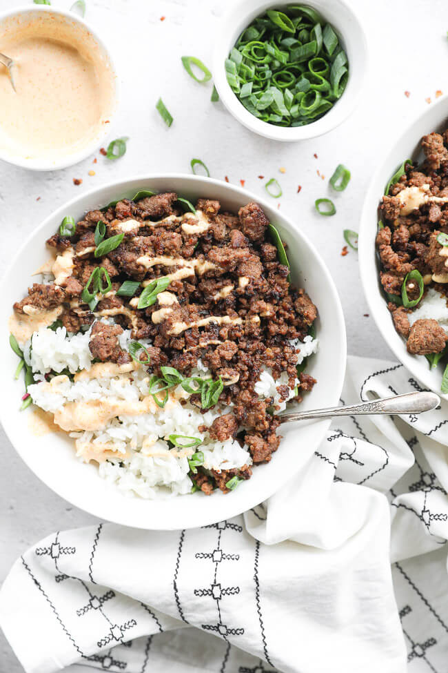 Korean beef served in a bowl with rice and greens. Topped with chopped green onion and drizzled with spicy mayo. 