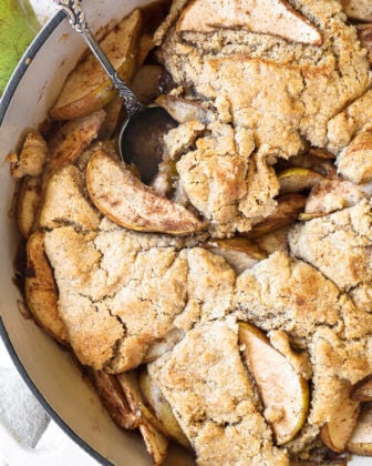 Vertical overhead close up image of pear cobbler in a skillet with a serving spoon dug in.