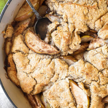 Vertical overhead close up image of pear cobbler in a skillet with a serving spoon dug in.