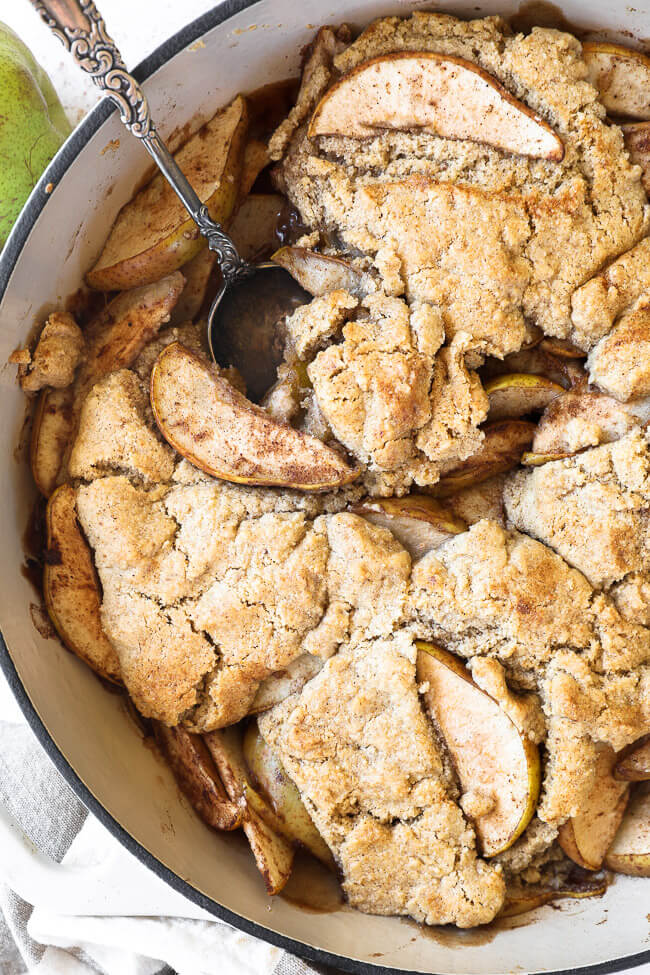 Vertical overhead close up image of pear cobbler in a skillet with a serving spoon dug in. 