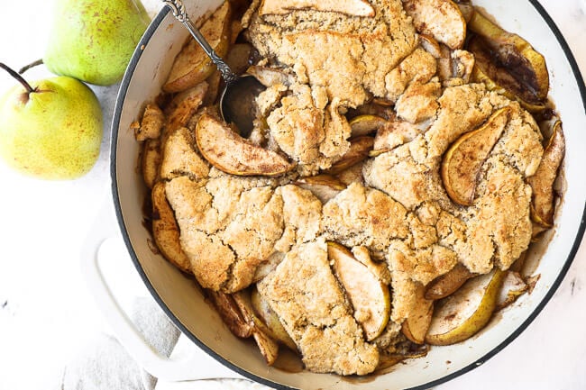 Horizontal overhead image of pear cobbler in a skillet with a serving spoon dug in. 