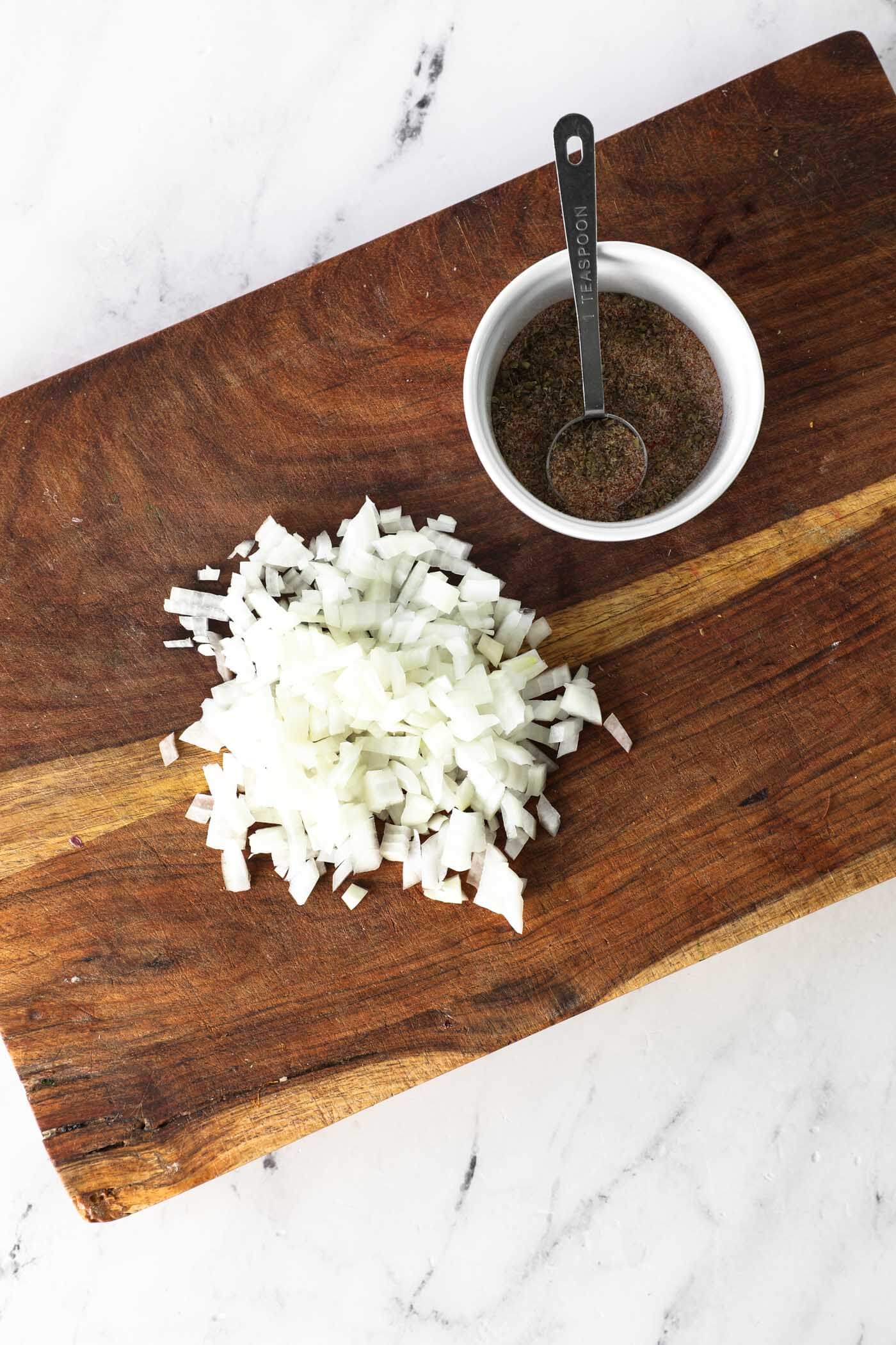 Overhead image of chopped onion on a cutting board with a ramekin of seasonings.