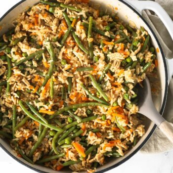 Close up overhead image of ground chicken and rice with veggies in a skillet with a serving spoon.