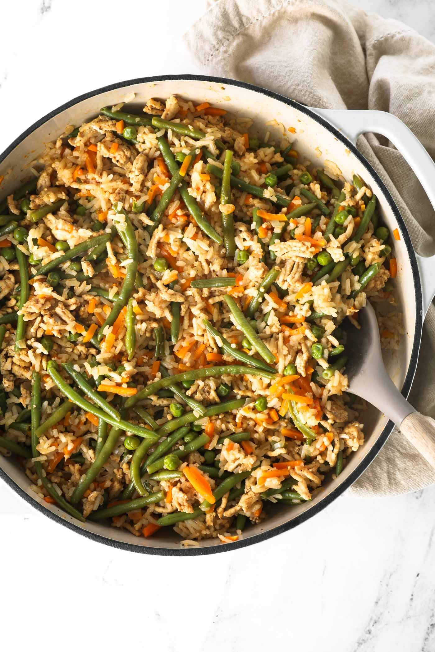 Close up overhead image of ground chicken and rice with veggies in a skillet with a serving spoon.