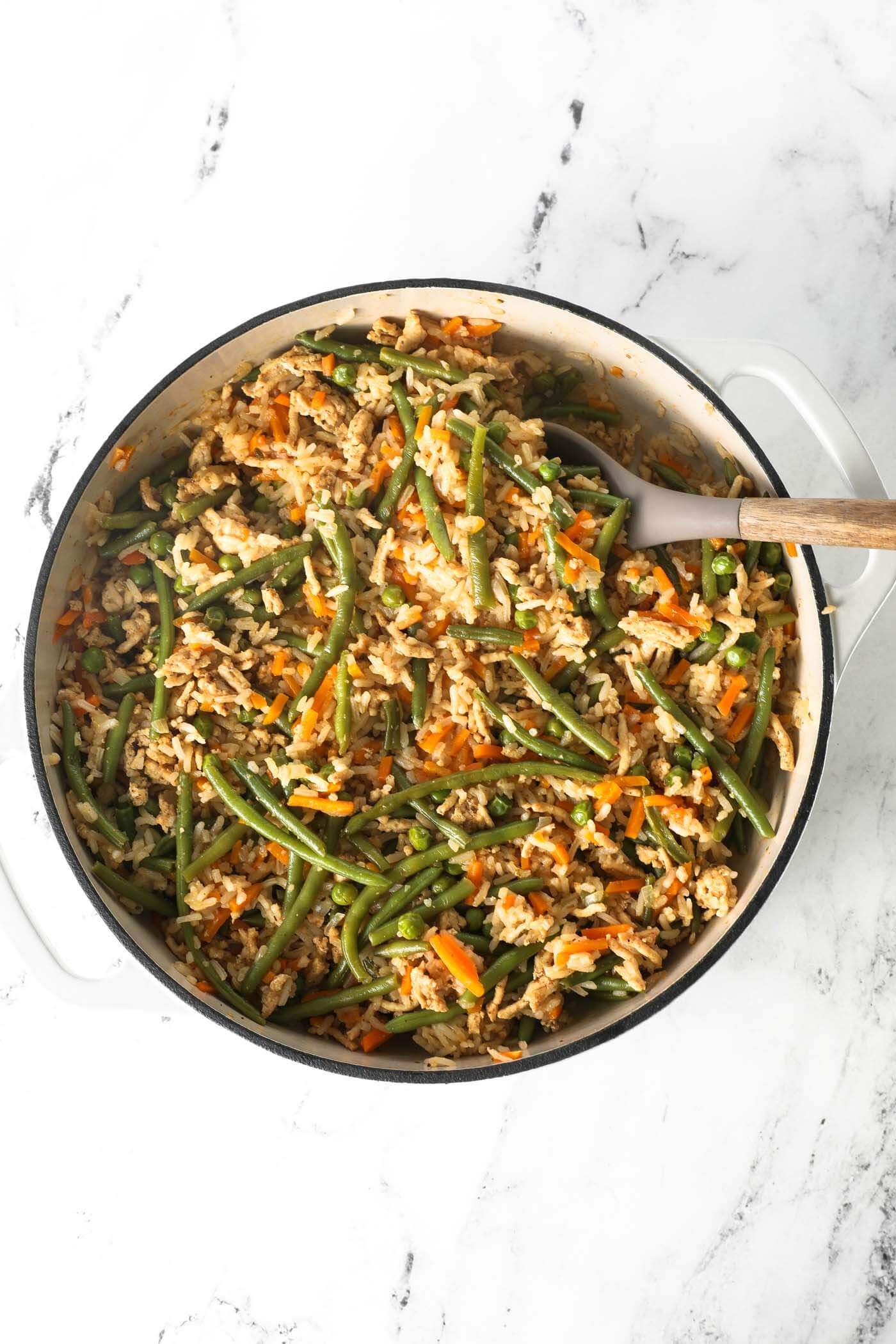 Overhead image of the cooked ground chicken and rice with veggies meal in a skillet with a serving spoon.