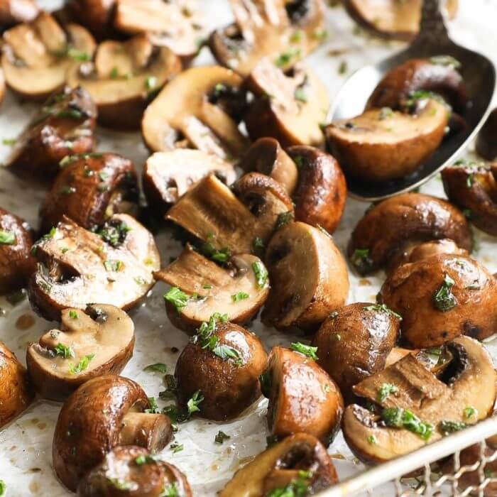 Vertical angled close up image of mushrooms in air fryer basket, so you can see the melted ghee and fresh herb mixture.