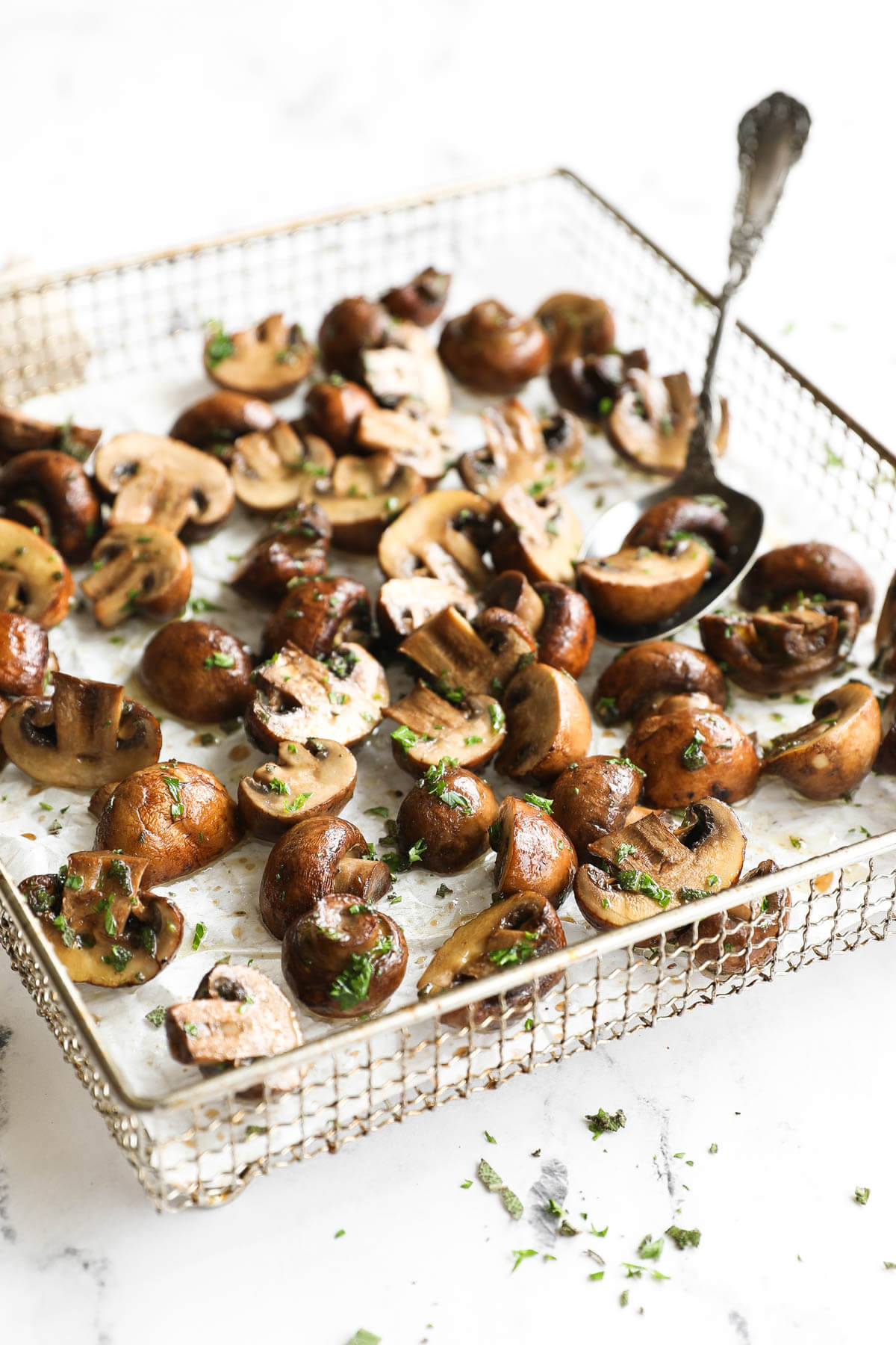 Vertical angled image of mushrooms in air fryer basket, so you can see the melted ghee and fresh herb mixture.