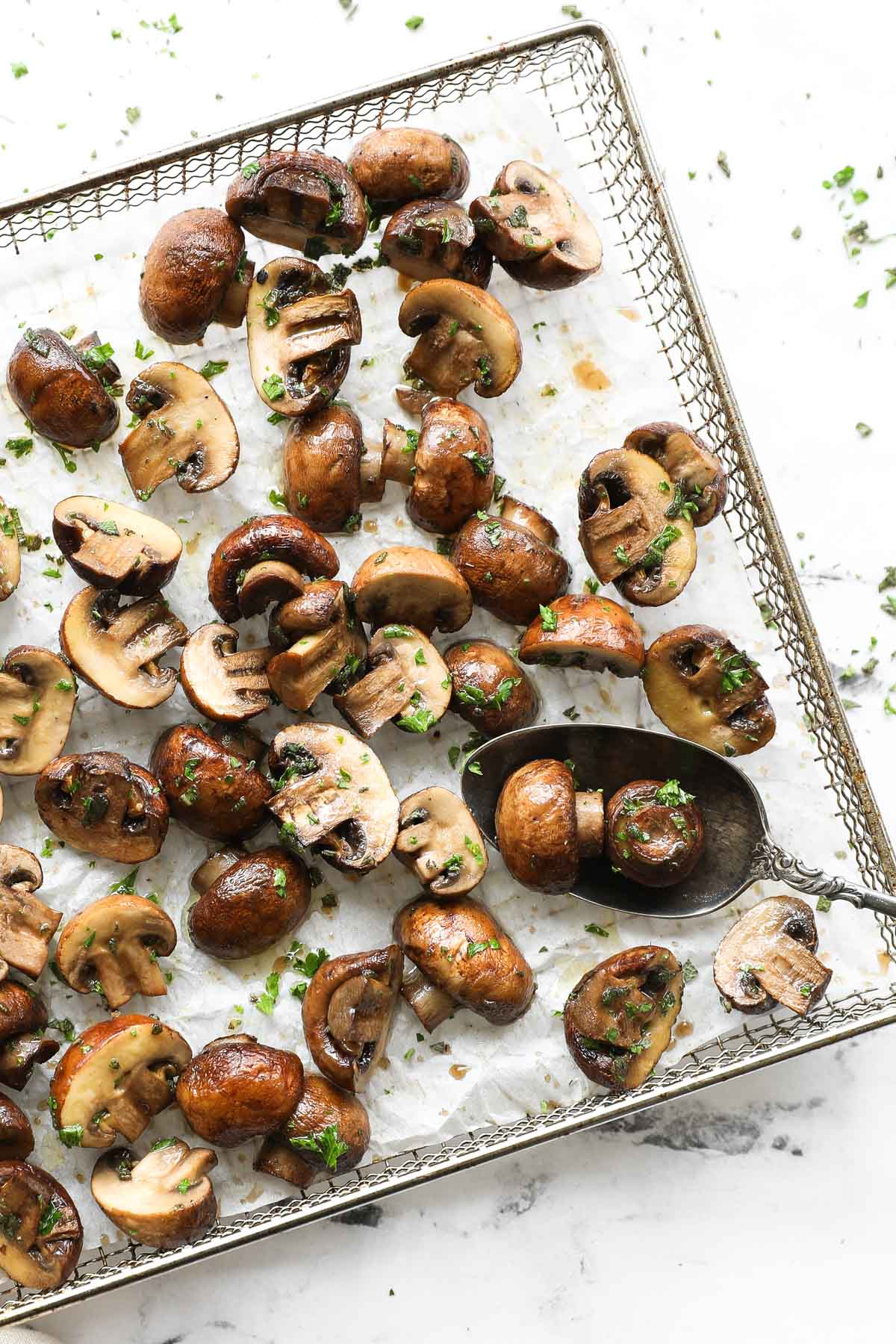Vertical overhead image of mushrooms in air fryer basket with a serving spoon.