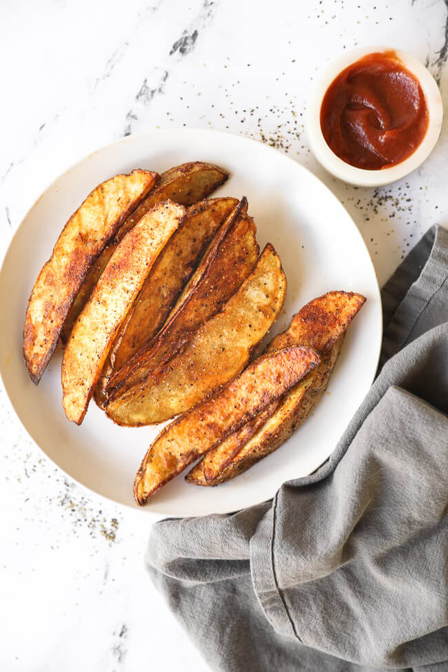 Overhead image of air fryer potato wedges lined up on a plate. 