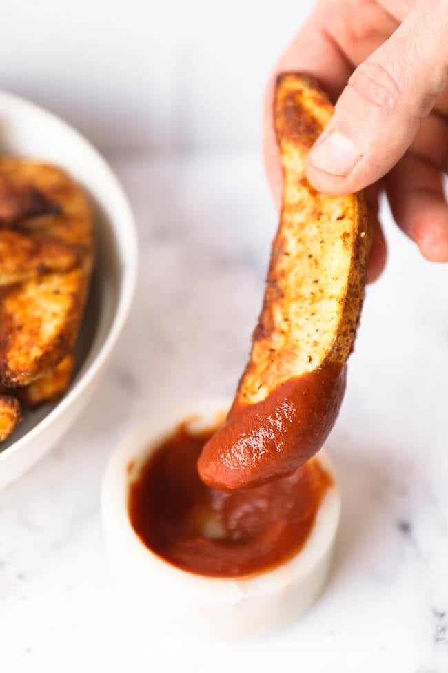 Angled image of dipping one air fryer potato wedge into ketchup. 