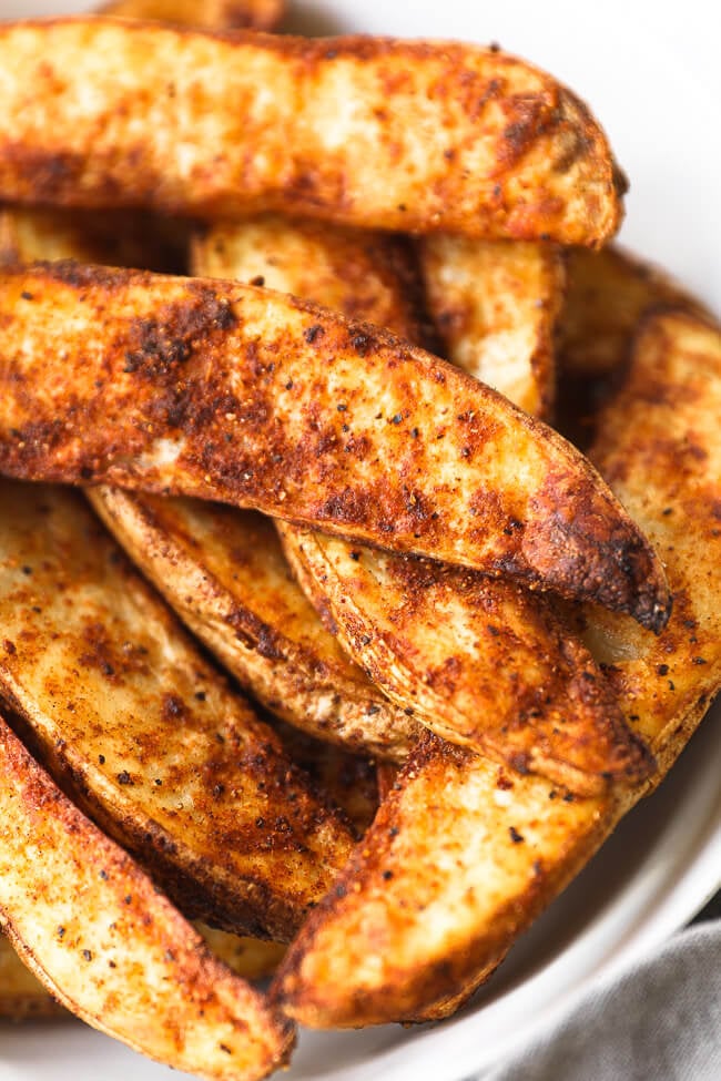 Close up angled image of crispy air fryer potato wedges in a bowl. 