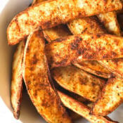 Close up image of air fryer potato wedges in a bowl. You can see the crispy edges and seasonings.