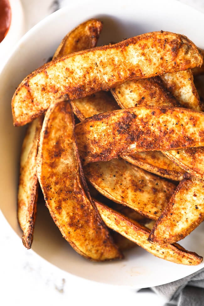 Vertical close up overhead image of air fryer potato wedges piled in a bowl. 