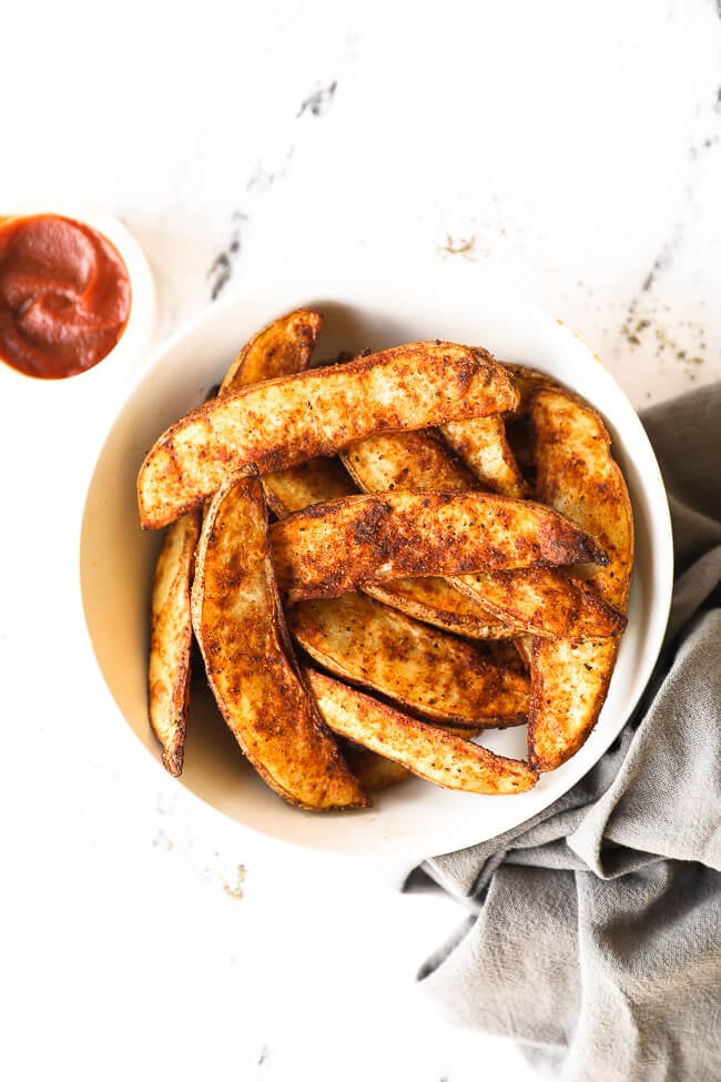 Overhead image of air fryer potato wedges piled in a bowl with ketchup on the side. 