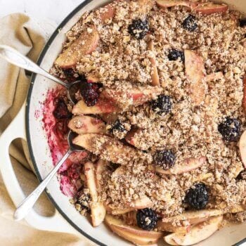 Overhead image of a blackberry and apple crumble in a skillet with two spoons dug in.