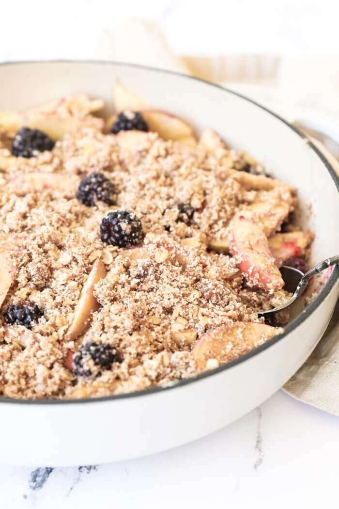 Angled image of blackberry and apple crumble in a skillet to show the crumbly texture of the topping.