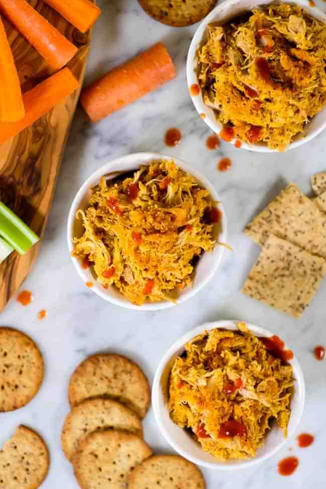 Healthy buffalo chicken dip in ramekins with hot sauce, crackers, carrots and celery. 