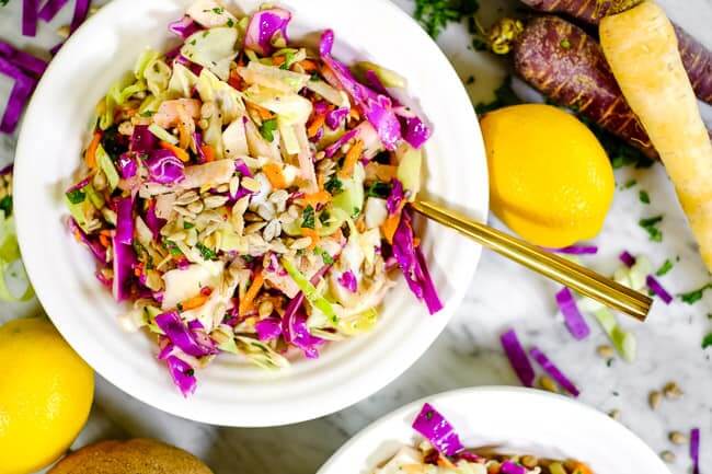 Healthy coleslaw in a bowl with lemon, carrots and cabbage on the table.