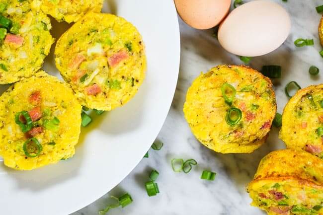 egészséges tojás muffin egy tányéron és az asztalon tojással és apróra vágott zöldhagymával.