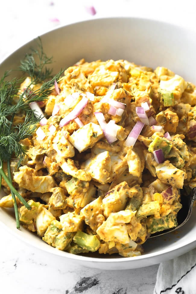 Close up of healthy egg salad in a bowl with chopped red onion on top and fresh dill garnish. 