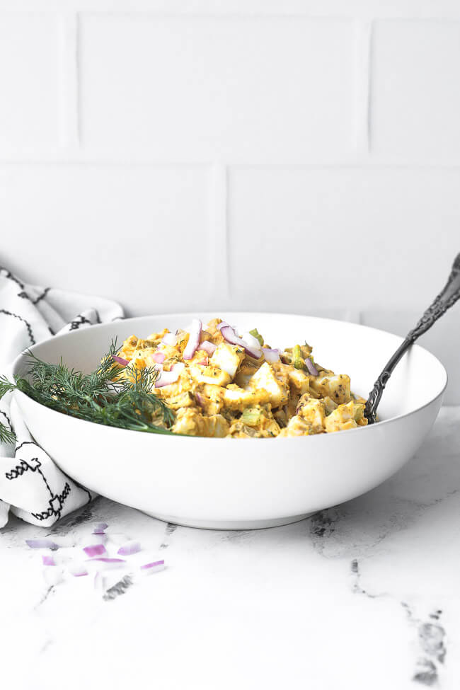 Straight on image of egg salad in a white bowl with spoon sticking out