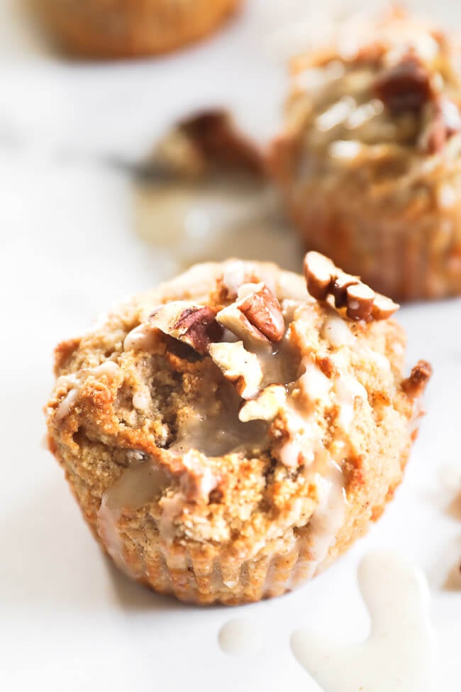 Close up image of one vegan, gluten free banana muffin. Drizzled with maple glaze and topped with chopped pecans. 