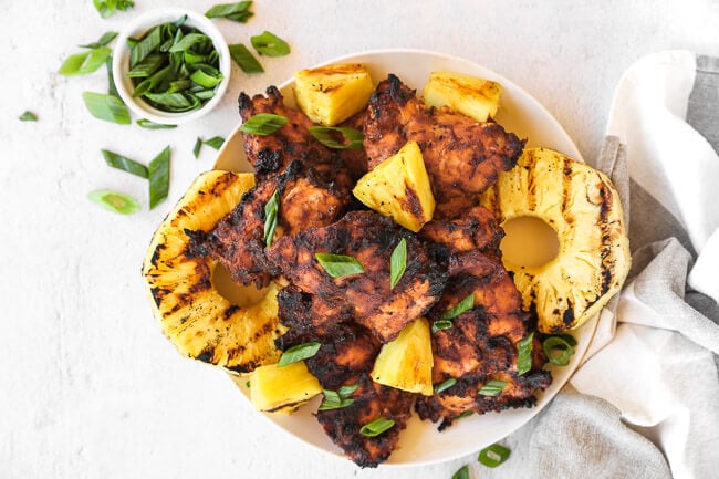 Grilled chicken and pineapple on a plate with chopped green onion sprinkled on top. 